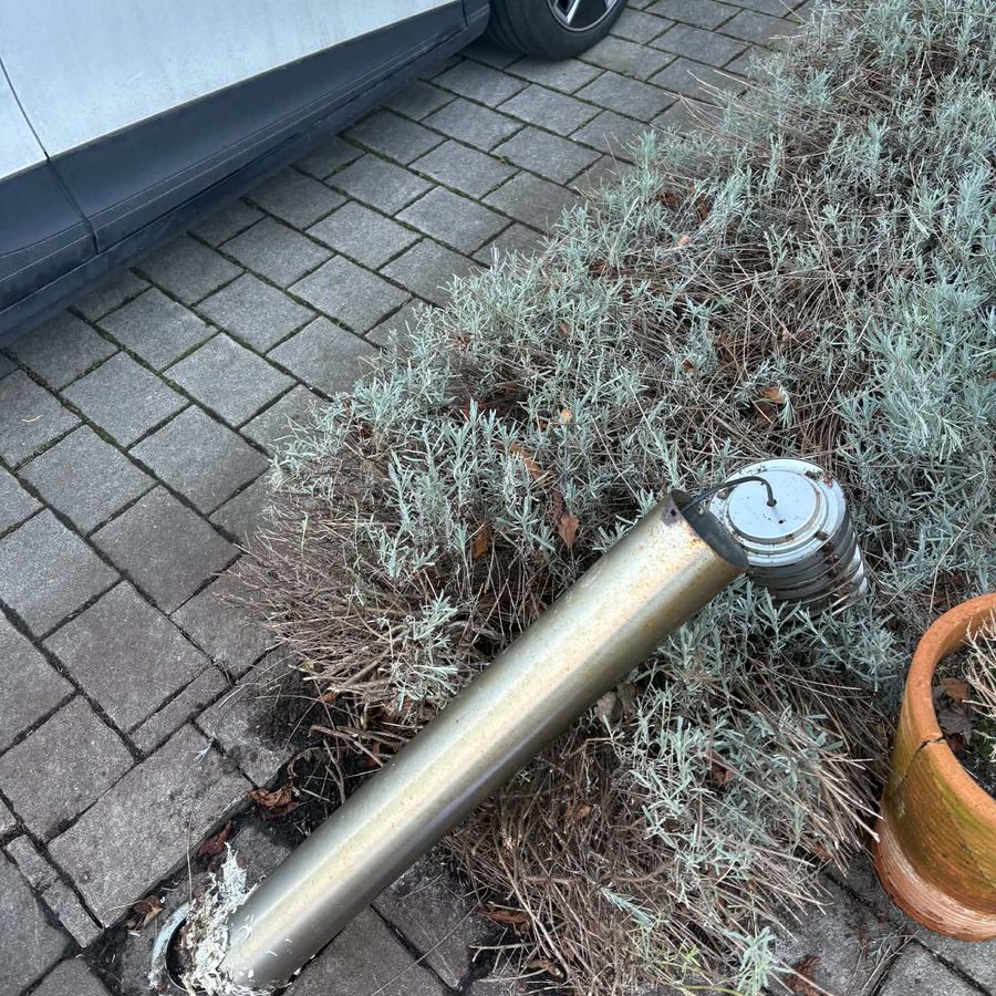 A corroded bollard light snapped off at its base, lying in a lavender bed beside a driveway
