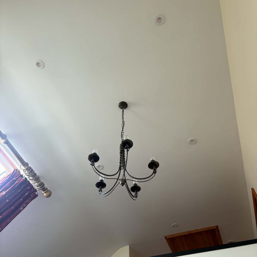 A dark iron five-arm chandelier hanging in a tall stairwell