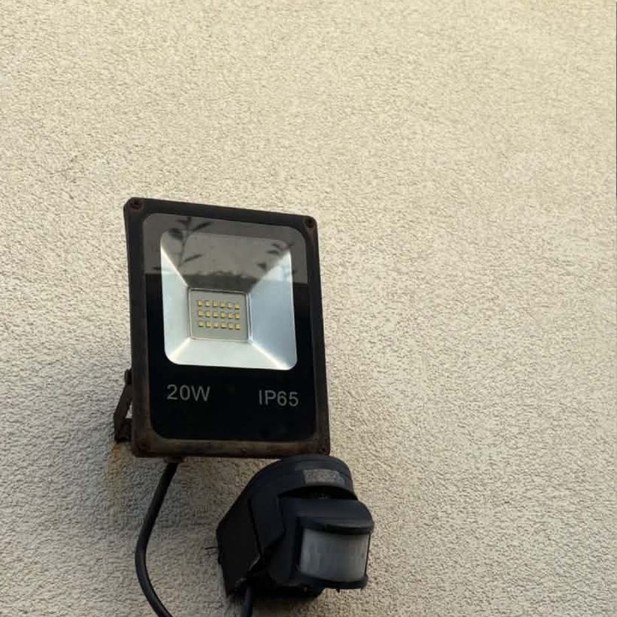 A rusted 20W LED floodlight and old PIR sensor on a pebbledash wall