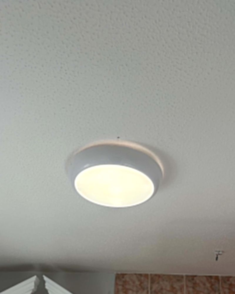 A round white flush ceiling light, lit, on a bathroom ceiling