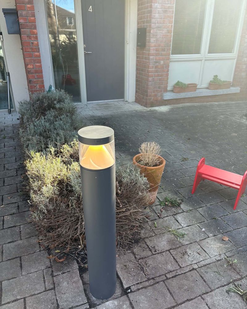 A lit bollard light beside a front door and planted bed