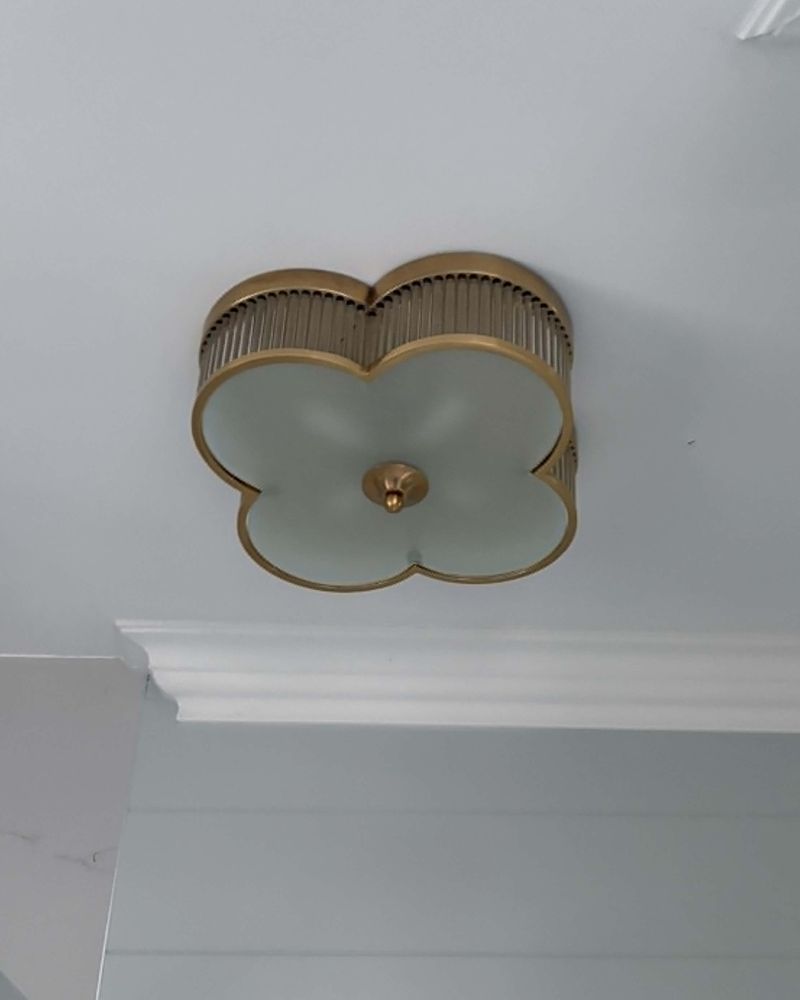 A brass flush fitting with a frosted clover-shaped shade on a bathroom ceiling