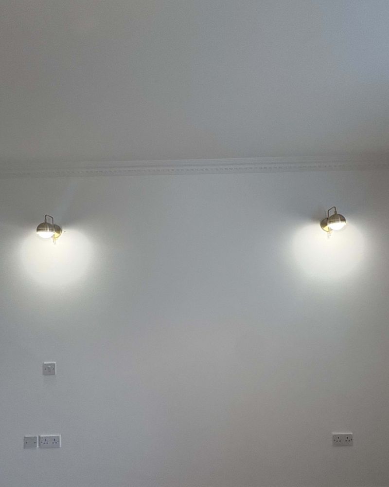 A pair of brass wall lights lit either side of a wall below coving