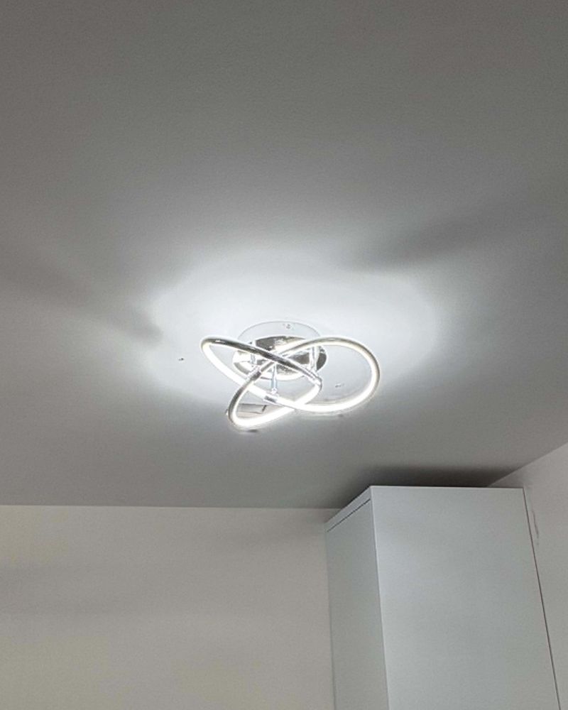 A chrome looped LED ceiling fitting, lit, on a white ceiling