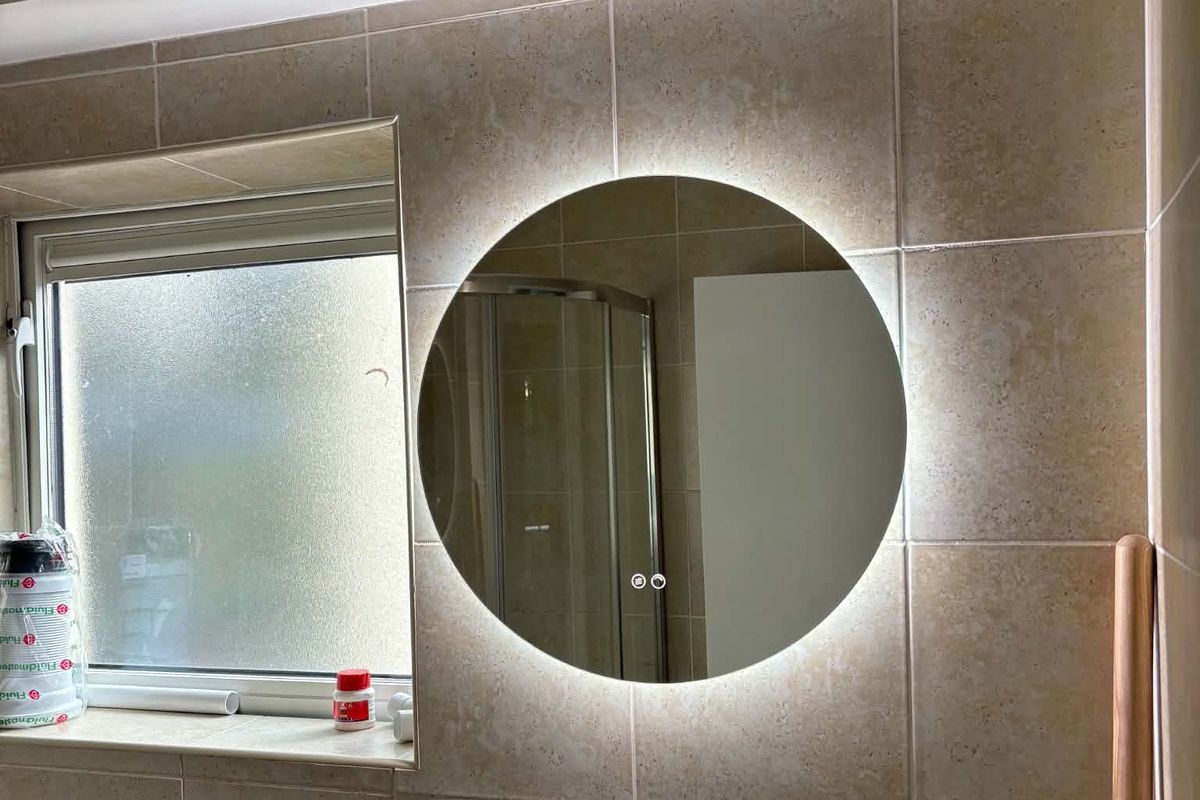 A backlit round LED mirror fitted on a tiled bathroom wall