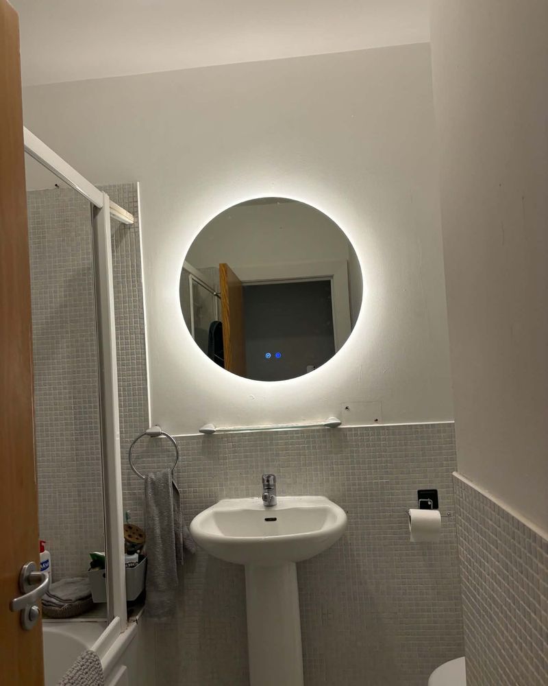 A backlit round LED mirror fitted above a bathroom sink